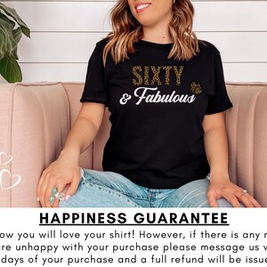 May include: Black t-shirt with gold glitter text that reads "SIXTY & Fabulous". The shirt is being worn by a person sitting on a pink couch. The text "HAPPINESS GUARANTEE" is at the bottom of the image.