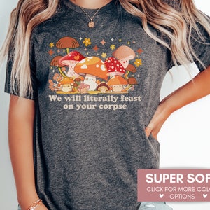 Op de afbeelding: Een donkergrijs T-shirt met een cartoon-paddenstoelontwerp en de tekst "We will literally feast on your corpse".