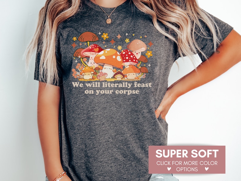 Op de afbeelding: Een donkergrijs T-shirt met een cartoon-paddenstoelontwerp en de tekst "We will literally feast on your corpse".