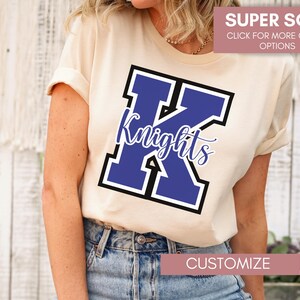 Puede incluir: Una camiseta blanca con una letra K azul y negra y la palabra "Knights" impresa en ella. La camiseta es s&uacute;per suave y personalizable.