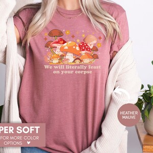 Op de afbeelding: Een heide-paarse t-shirt met een cartoon-paddenstoelmotief en de tekst "We will literally feast on your corpse".