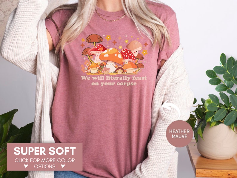 Op de afbeelding: Een heide-paarse t-shirt met een cartoon-paddenstoelmotief en de tekst "We will literally feast on your corpse".