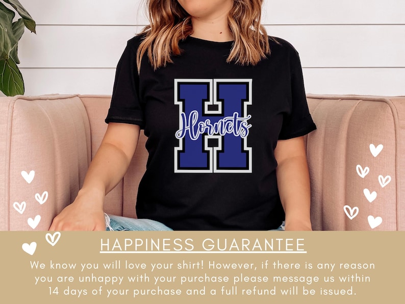 Puede incluir: Camiseta negra con una gran letra "H" azul y blanca con la palabra "Hornets" escrita en blanco dentro de la letra. La camiseta la lleva puesta una persona sentada en un sof&aacute; rosa. El texto "Happiness Guarantee" est&aacute; en la parte inferior de la imagen.