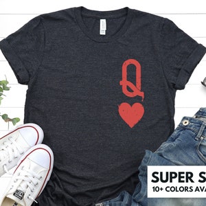 May include: A dark gray t-shirt with a red queen of hearts playing card graphic. The text "SUPER SOFT" and "10+ COLORS AVAILABLE" is printed on the bottom of the image.