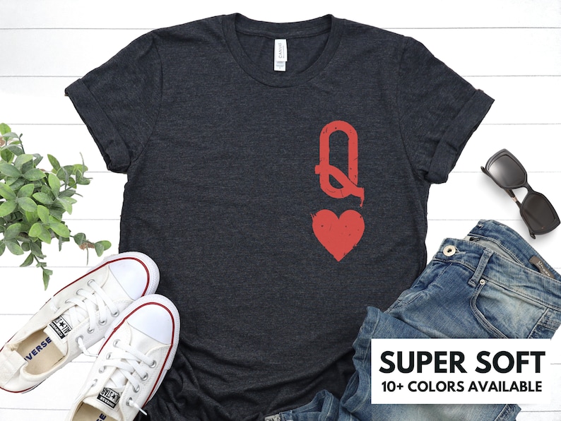 May include: A dark gray t-shirt with a red queen of hearts playing card graphic. The text "SUPER SOFT" and "10+ COLORS AVAILABLE" is printed on the bottom of the image.