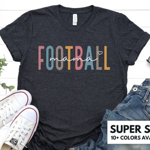 Op de afbeelding: Een donkergrijs t-shirt met de tekst "FOOTBALL mama" in regenboogkleuren met een klein hartje na het woord "mama".