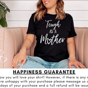 K&ouml;nnte beinhalten: Ein schwarzes T-Shirt mit wei&szlig;em Text, der "Tough as a Mother" lautet, wobei ein kleines Herz das "o" in Mother ersetzt. Das Shirt wird von einer Person getragen, die auf einem rosa Sofa sitzt. Der Text "Happiness Guarantee" befindet sich am unteren Rand des Bildes. Wir wissen, dass Sie Ihr Shirt lieben werden! Wenn Sie jedoch aus irgendeinem Grund mit Ihrem Kauf nicht zufrieden sind, kontaktieren Sie uns bitte innerhalb von 14 Tagen nach Ihrem Kauf, und wir erstatten Ihnen den vollen Kaufpreis.