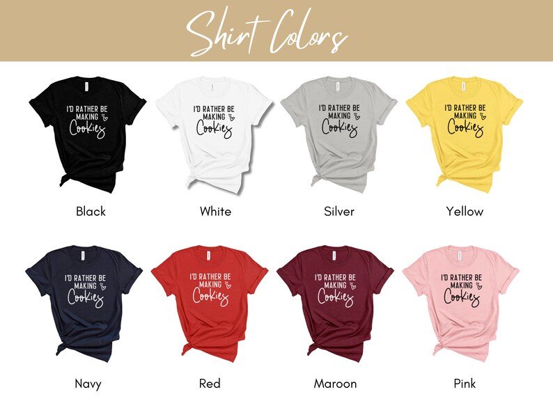 May include: A mockup of a t-shirt design showing different color options. The shirt design features the text "I'd rather be making cookies" in black text with a heart and the word "cookies" in white text. The colors shown are black, white, silver, yellow, navy, red, maroon, and pink.