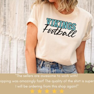 May include: A white t-shirt with a blue and black graphic that says "VIKINGS Football". The shirt is being worn by a person with long brown hair. The text below the image says "The sellers are awesome to work with! Shipping was amazingly fast! The quality of the shirt is superb! I will be ordering from this shop again!"