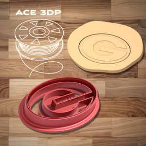 Puede incluir: Un cortador de galletas de plástico rojo en forma de la letra "G" con un doble contorno. El cortador de galletas está sobre una superficie de madera.