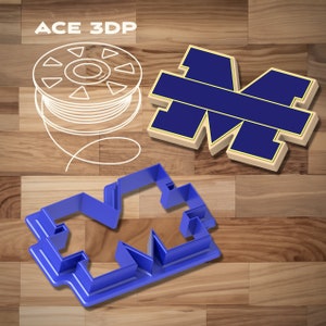 May include: Blue plastic cookie cutter shaped like the letter M. The cutter is on a wooden surface with a spool of white filament and a blue and gold M on a white background.