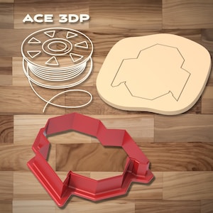 Può includere: Tagliapasta in plastica rossa a forma di casa con tetto arrotondato. Il tagliapasta è su una superficie di legno.  ACE 3DP è scritto in bianco sulla superficie di legno.