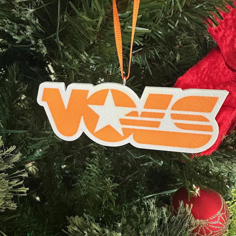 Puede incluir: Adorno navide&ntilde;o naranja y blanco con la palabra "VOLS" en una fuente retro. El adorno tiene una estrella blanca en el centro de la "O".