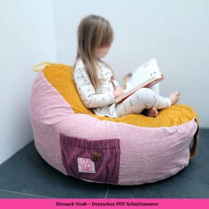 May include: A pink and mustard yellow beanbag chair with a small purple pocket that says "Love This" and has a bee embroidered on it. A young girl is sitting in the chair reading a book.