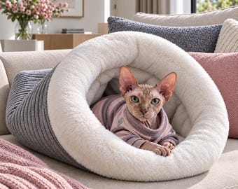 May include: A hairless cat wearing a pink and grey striped sweater resting inside a grey and white tunnel-shaped pet bed. The bed features a ribbed grey exterior and a soft, plush white interior lining, providing a cozy space for the cat.