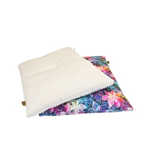 May include: Two decorative pillows. The top pillow is a cream-colored, corduroy-textured square. The bottom pillow features a vibrant floral pattern with pink, blue, and purple flowers on a dark background. Both pillows are square.