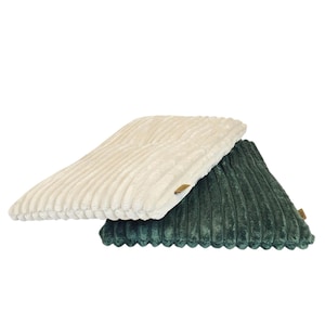 May include: Two corduroy pillows, one cream and the other dark green, are stacked. The pillows have a ribbed texture and small rectangular tags. These soft pillows are a neutral addition to any home decor.