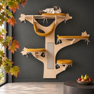 May include: A wall-mounted cat tree made of light-colored wood with multiple platforms and a hammock. The structure features mustard yellow cushions tied to the shelves with white cords, maple leaf-shaped accents, and a vertical scratching post.