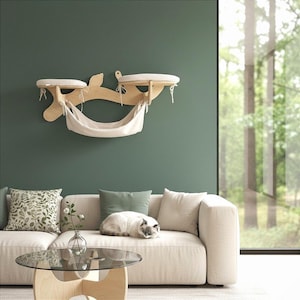 May include: A wooden cat shelf with two circular platforms and a hammock, mounted on a green wall. The platforms have striped cushions. A cat rests on a beige sofa below. The room has a modern design with a glass coffee table.