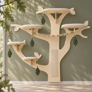 May include: A wall-mounted cat tree made of light-colored wood, featuring five circular platforms with white cushions, a central woven scratching panel, a suspended rope bridge, and several hanging dark green felt oak leaf decorations.
