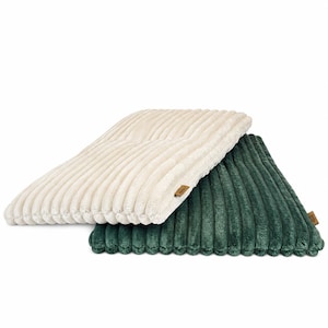 Pode incluir: Duas almofadas retangulares com uma textura macia de veludo cotelê. Uma almofada de cor creme está sobreposta a uma almofada verde-floresta escura. Cada almofada apresenta uma pequena etiqueta retangular de tecido castanho na lateral.