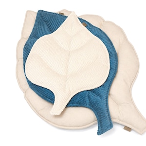 Op de afbeelding: Een set van drie bladvormige kussens in verschillende maten en texturen. De grootste is lichtbeige, de middelste is teal corduroy en de kleinste is off-white met een textuur. De kussens zijn in een gelaagd patroon gerangschikt.
