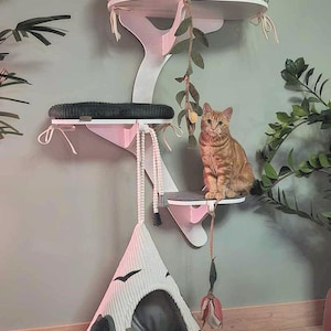 May include: A white wall-mounted cat tree with multiple levels, featuring a top platform with a botanical print cushion, a middle platform with a dark gray cushion, and a hanging white cone-shaped fabric cat bed with black bird graphics.
