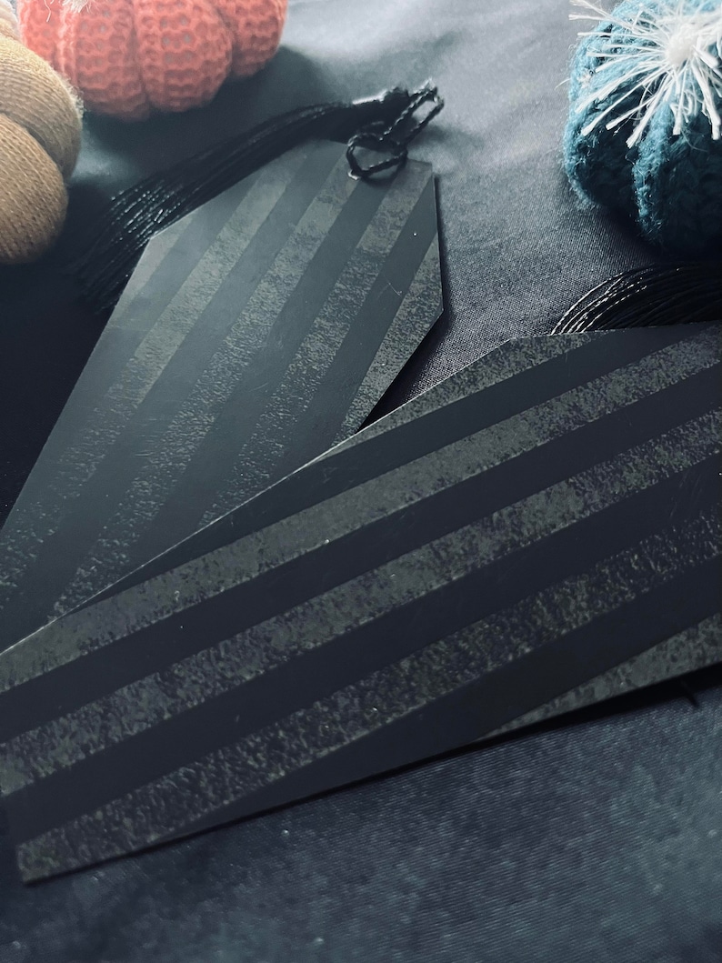 May include: Two black striped gift tags with a black string attached to the top. The tags are shaped like a coffin.
