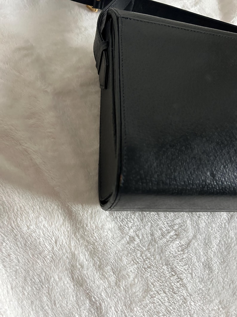 May include: A black rectangular handbag with a shoulder strap. The bag is made of a smooth, possibly leather material. The strap is thin and appears to be adjustable. The bag is closed with a flap.
