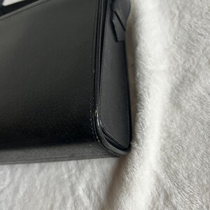 May include: A black rectangular handbag with a structured design. The bag has a smooth, matte finish and a visible seam detail along the edges. The bag's corner is slightly rounded.