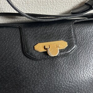May include: Black leather handbag with a gold-tone clasp. The handbag features a textured surface and a shoulder strap. The clasp is rectangular with the words "valentino garavani" engraved on it.