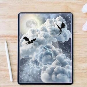Puede incluir: Una tableta digital muestra una escena de fantasía de dragones volando a través de un cielo tormentoso con luna llena. Un lápiz óptico blanco y flores rosas y blancas están junto a la tableta sobre una superficie de madera.