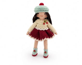 May include: A handcrafted doll with dark brown yarn hair, wearing a light green crocheted beret with a red pom-pom, a cream-colored long-sleeved top with a small cherry accent, a deep red skirt with a scalloped hem, and matching light green boots.
