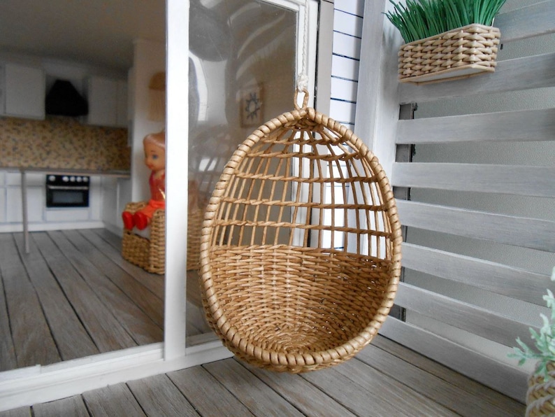 May include: A brown wicker hanging chair with a woven design. The chair is hanging from a white ceiling in a dollhouse.