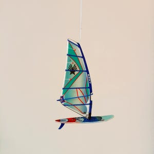 Puede incluir: Una vela de windsurf azul y blanca con detalles rojos colgando del techo. La vela está etiquetada como "Ezzy" y tiene un logotipo de estrella.