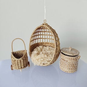 May include: Three woven wicker baskets, one hanging from the ceiling, one on wheels, and one with a lid. The hanging basket is a round chair with a white fluffy cushion inside.