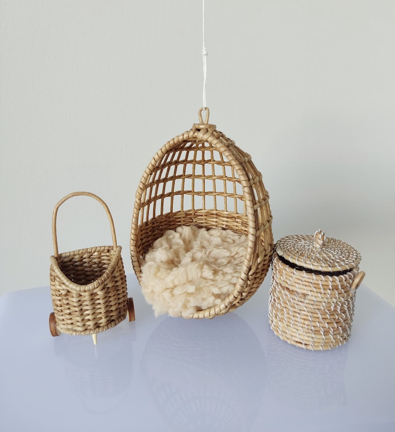 May include: Three woven wicker baskets, one hanging from the ceiling, one on wheels, and one with a lid. The hanging basket is a round chair with a white fluffy cushion inside.