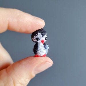 May include: A small crocheted penguin holding a smaller crocheted penguin. The penguin is black and white with red feet and a red beak.