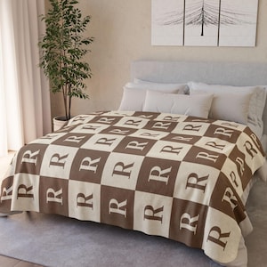 May include: A brown and cream checkered throw blanket with the letter "R" repeated in a pattern.