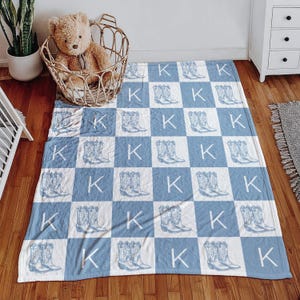 Peut inclure: Une couverture en polaire à carreaux bleus et blancs avec un contour blanc de bottes de cow-boy et la lettre "K" répétée sur tout le motif.