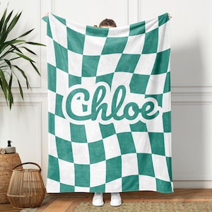 Op de afbeelding: Een teal en wit geruite fleece deken met de naam "Chloe" in een groen cursief schrift.