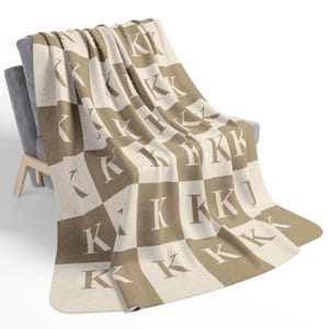 Può includere: Una coperta a quadri marroni e crema con la lettera "K" ripetuta in un motivo.