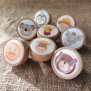 Könnte beinhalten: Acht Holzgriffe mit verschiedenen Tierillustrationen. Die Tiere sind ein Löwe, ein Koala, ein Pinguin, eine Giraffe, ein Stier, ein Elefant, ein Affe und ein Bär. Die Griffe sind alle rund und haben eine hellbraune Holzoptik.