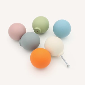 Może przedstawiać: Sześć drewnianych gałek w różnych kolorach: jasnozielonym, jasnoróżowym, jasnoniebieskim, szarym, białym i pomarańczowym. Gałki są okrągłe i mają śrubę na spodzie.