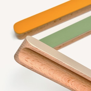 May include: Three wooden drawer pulls with different coloured paint finishes. The pulls are made of natural wood with a rounded edge and a recessed centre. The colours are a light yellow, a light green, and a light grey.