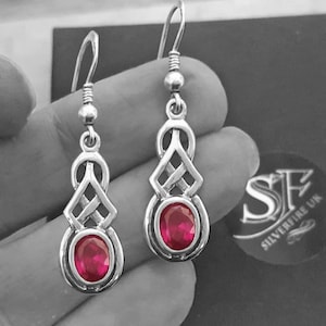 May include: Silver dangle earrings with a Celtic knot design and a pink oval gemstone.