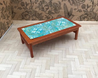 May include: A miniature wooden coffee table with a teal and white patterned tabletop. The table is sitting on a white wood floor.