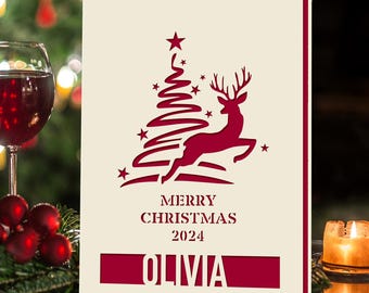 May include: A red and white Christmas card with a red reindeer jumping over a red Christmas tree with stars. The card says "Merry Christmas 2024" and "Olivia" at the bottom.