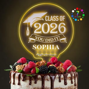 May include: A graduation cake with a light-up topper. The topper is a yellow circle with the text "CLASS OF 2026 YOU DID IT! SOPHIA" and a graduation cap graphic. The cake is decorated with berries and chocolate.