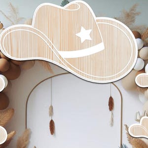 May include: Wooden cowboy hats with a white star design. The hats are arranged in a decorative archway with brown and beige balloons and dried grasses.